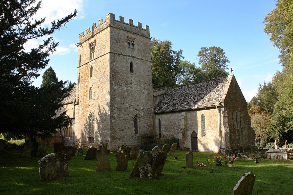 A historic church with a prominent tower and a smaller adjacent building, surrounded by a cemetery with headstones.