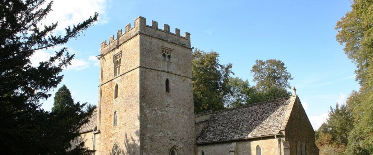 A historic church with a prominent tower and a smaller adjacent building, surrounded by a cemetery with headstones.
