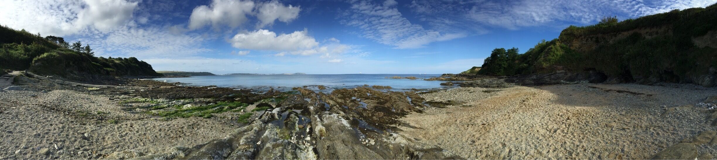 A coastal landscape with rocky shores, a sandy beach, and a clear view of the sea under a partly cloudy sky.