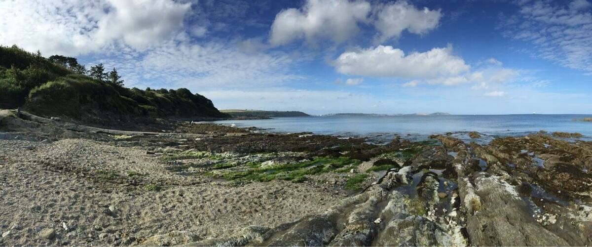 A coastal landscape with rocky shores, a sandy beach, and a clear view of the sea under a partly cloudy sky.