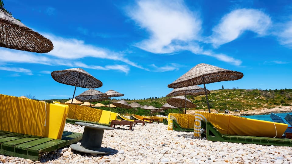 A pebble beach with umbrellas and lounge chairs.