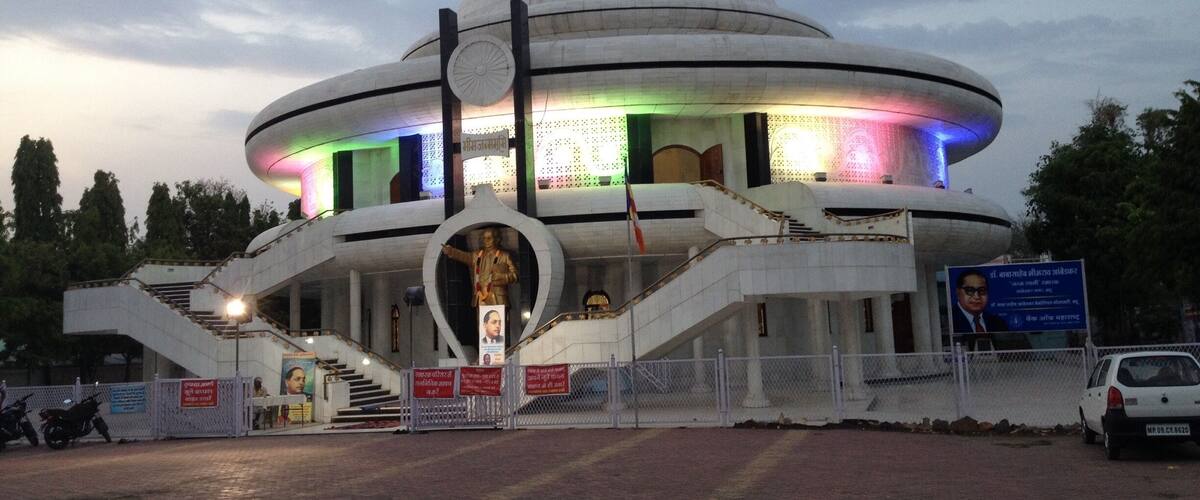 A large, dome-shaped building with a flag on top, surrounded by a fence and a statue in front.