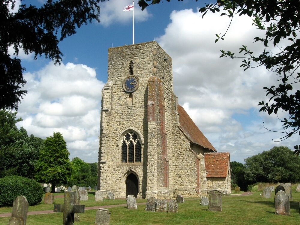 A stone church with a clock tower, surrounded by a cemetery with gravestones.
