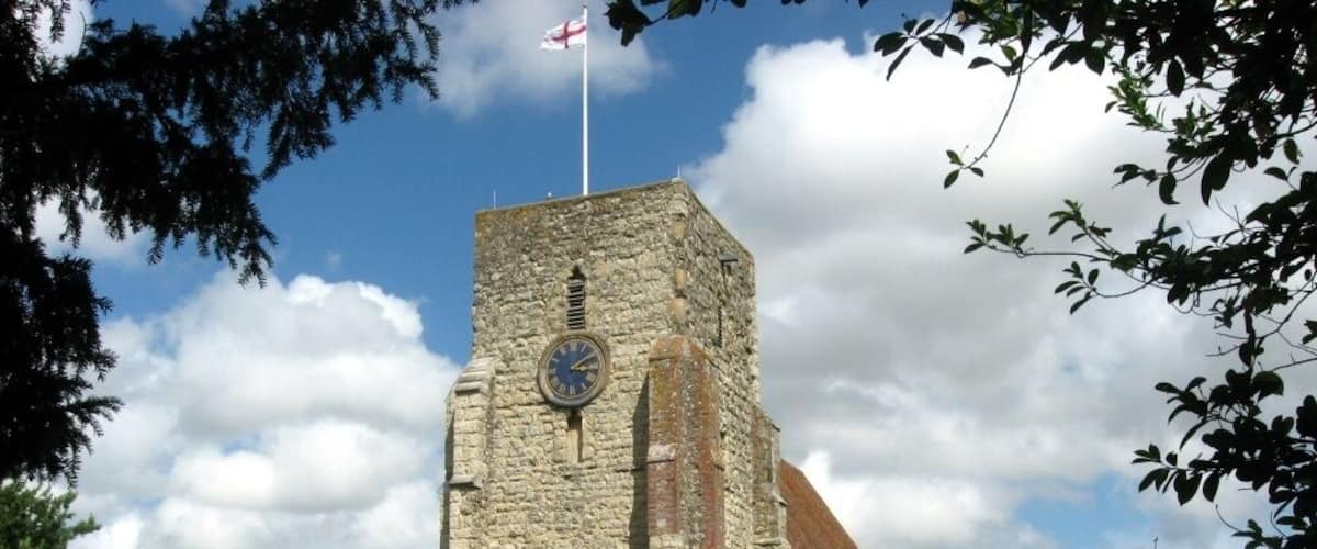 A stone church with a clock tower, surrounded by a cemetery with gravestones.