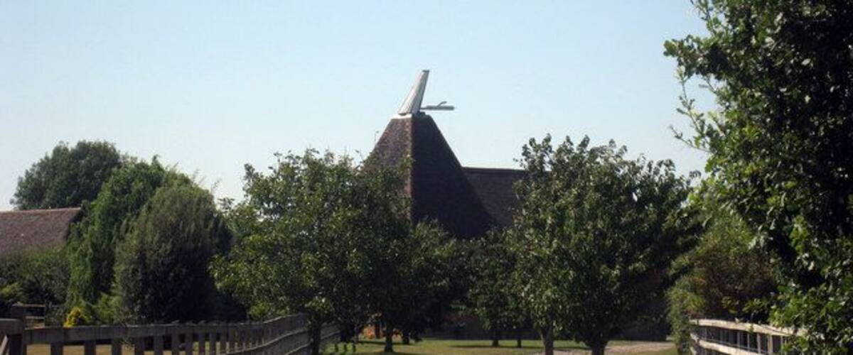A gravel path leading to a building with a pointed roof and a windmill in the background.