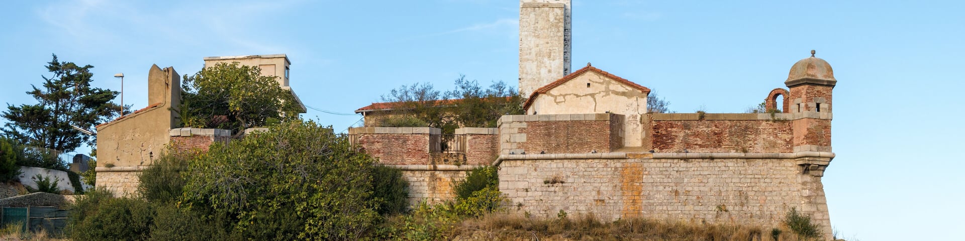 A historic fort with a prominent lighthouse, surrounded by greenery and rocky terrain.