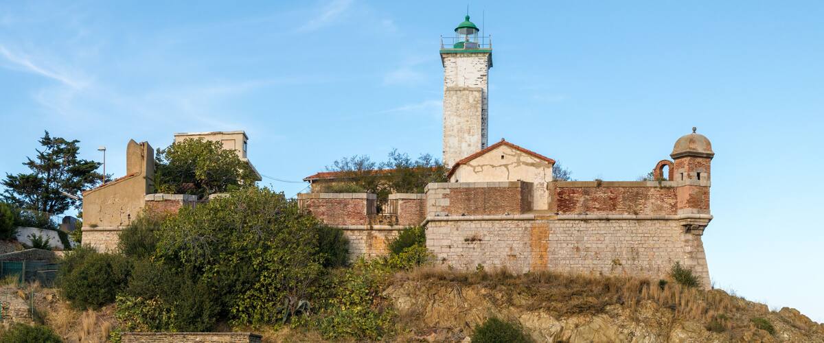 A historic fort with a prominent lighthouse, surrounded by greenery and rocky terrain.