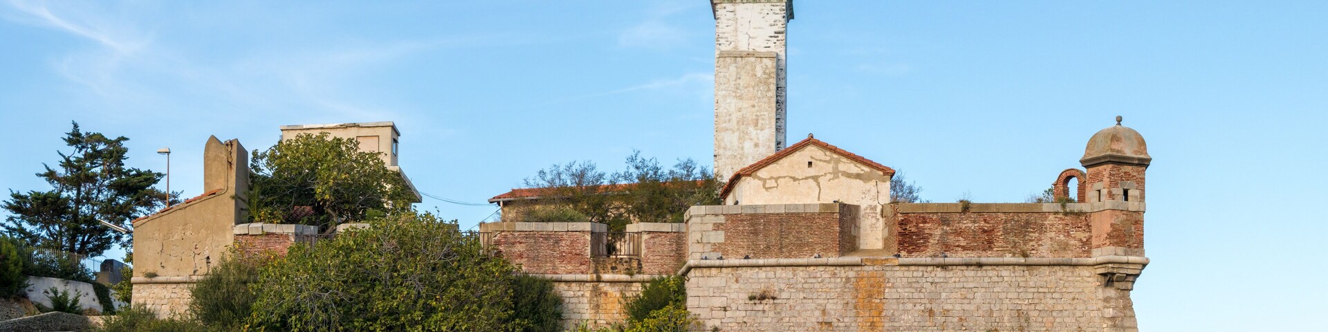 A historic fort with a prominent lighthouse, surrounded by greenery and rocky terrain.