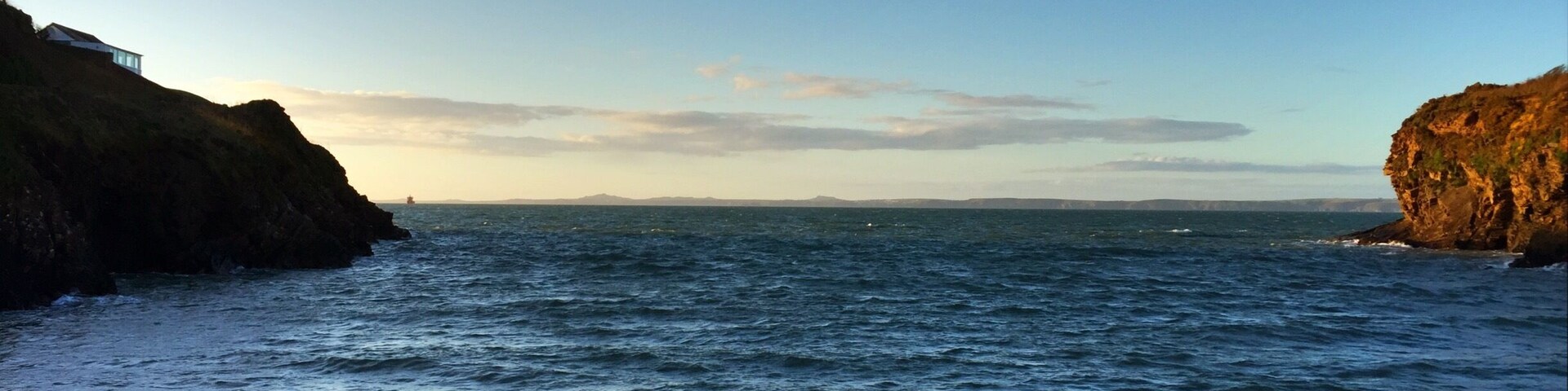 Un paisaje costero con un paseo marítimo de hormigón que lleva al mar, acantilados rocosos y un cielo despejado.