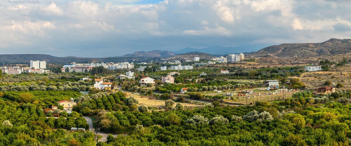 A coastal town with buildings, greenery, and mountains in the background.