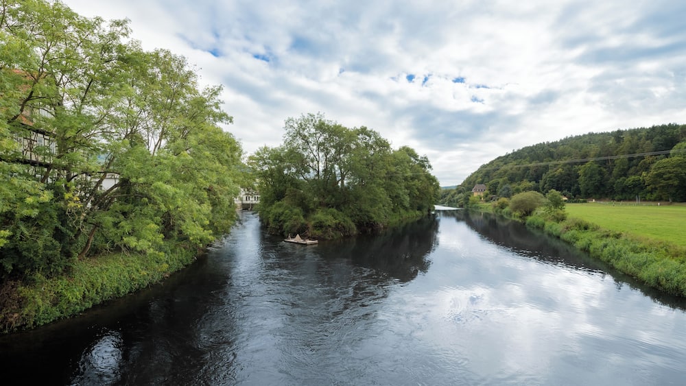 A river flanked by lush greenery and a bridge.