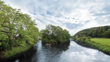 Die Werra bei Wanfried von der Wanfrieder Werrabrücke aus gesehen. Der linke Flussarm (Mühlgraben) dient zur Versorgung des Elektrizitätswerks Wanfried, dessen Gebäude im Hintergrund sichtbar ist. Vor der Insel in der Flussmitte ist ein Floß angelegt. Im linken Bildteil ist ein Teil der großen Schlagdhäuser zu sehen. Blickrichtung Süden.