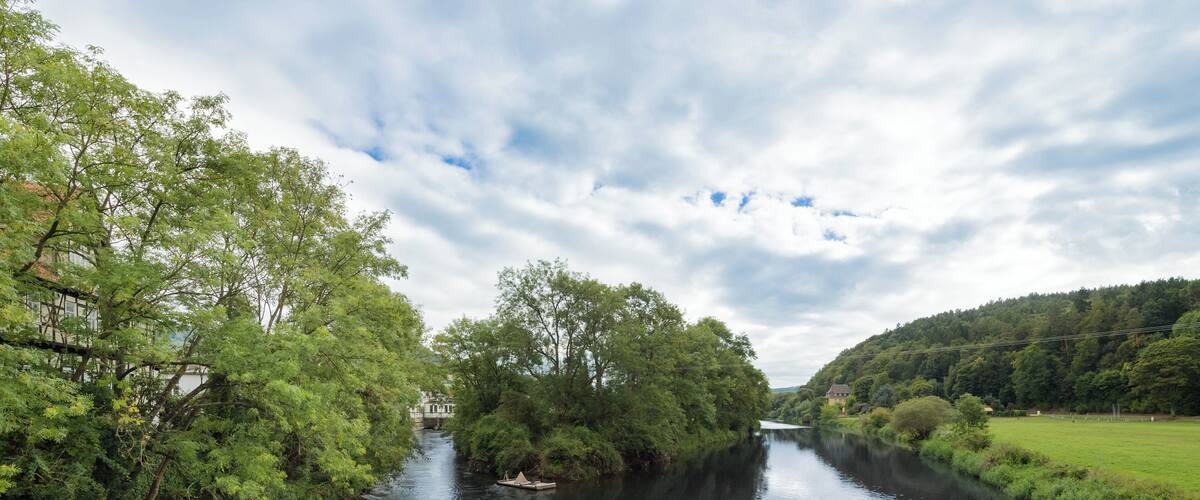 A river flanked by lush greenery and a bridge.
