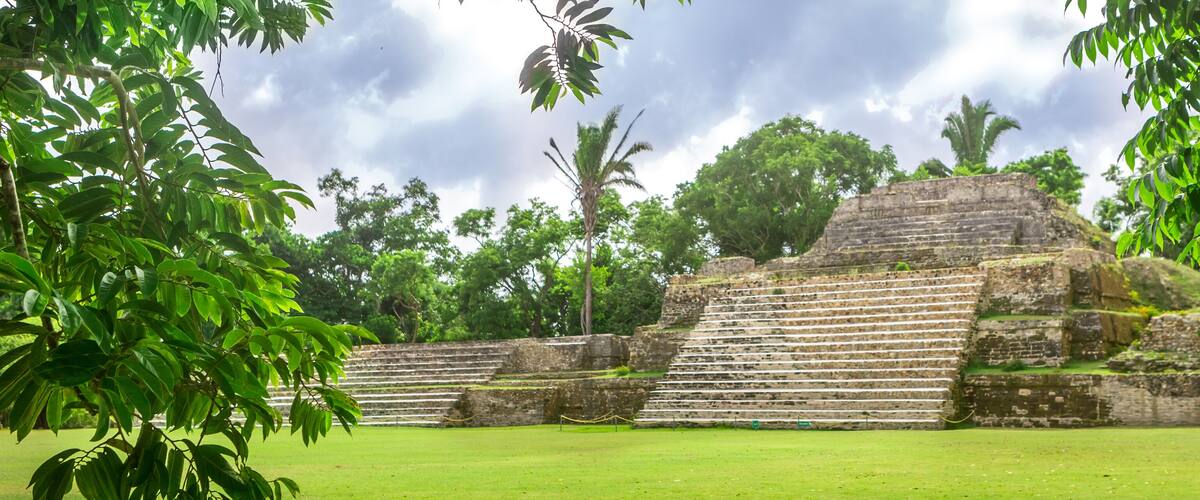 A large stone pyramid with steps, surrounded by lush green trees and grass.