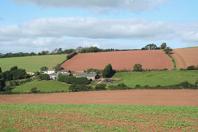 A rural landscape with rolling hills, fields, and a small cluster of houses.