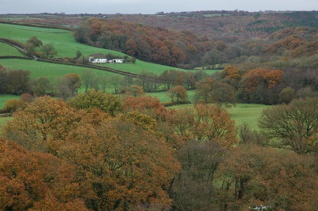 A rural landscape with rolling green fields, scattered trees, and a white house in the distance.