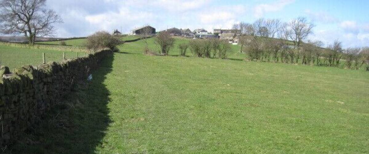 A stone wall, green field, and distant houses.