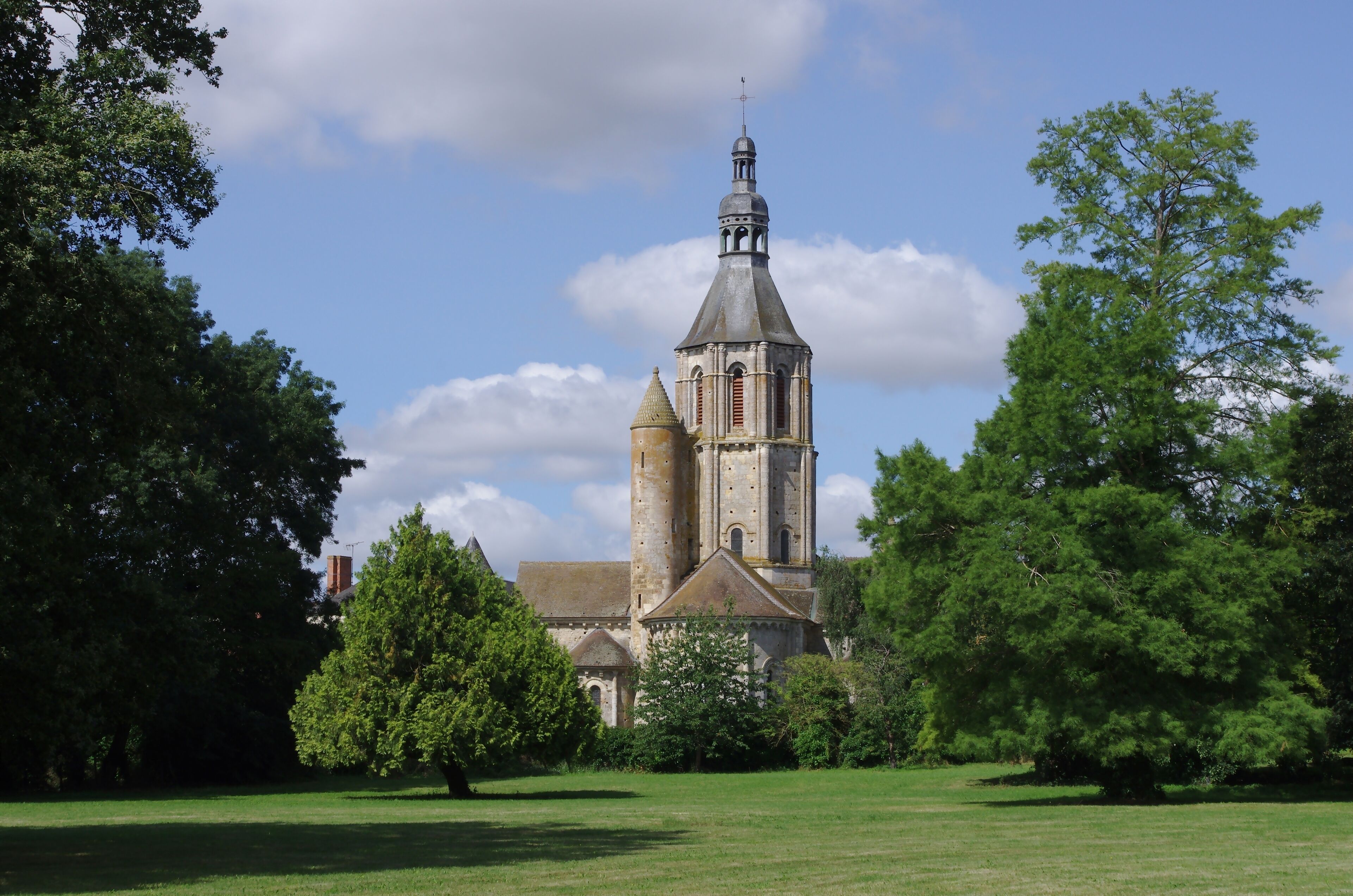 A historic church with a tall bell tower, surrounded by lush green trees and a well-maintained lawn.