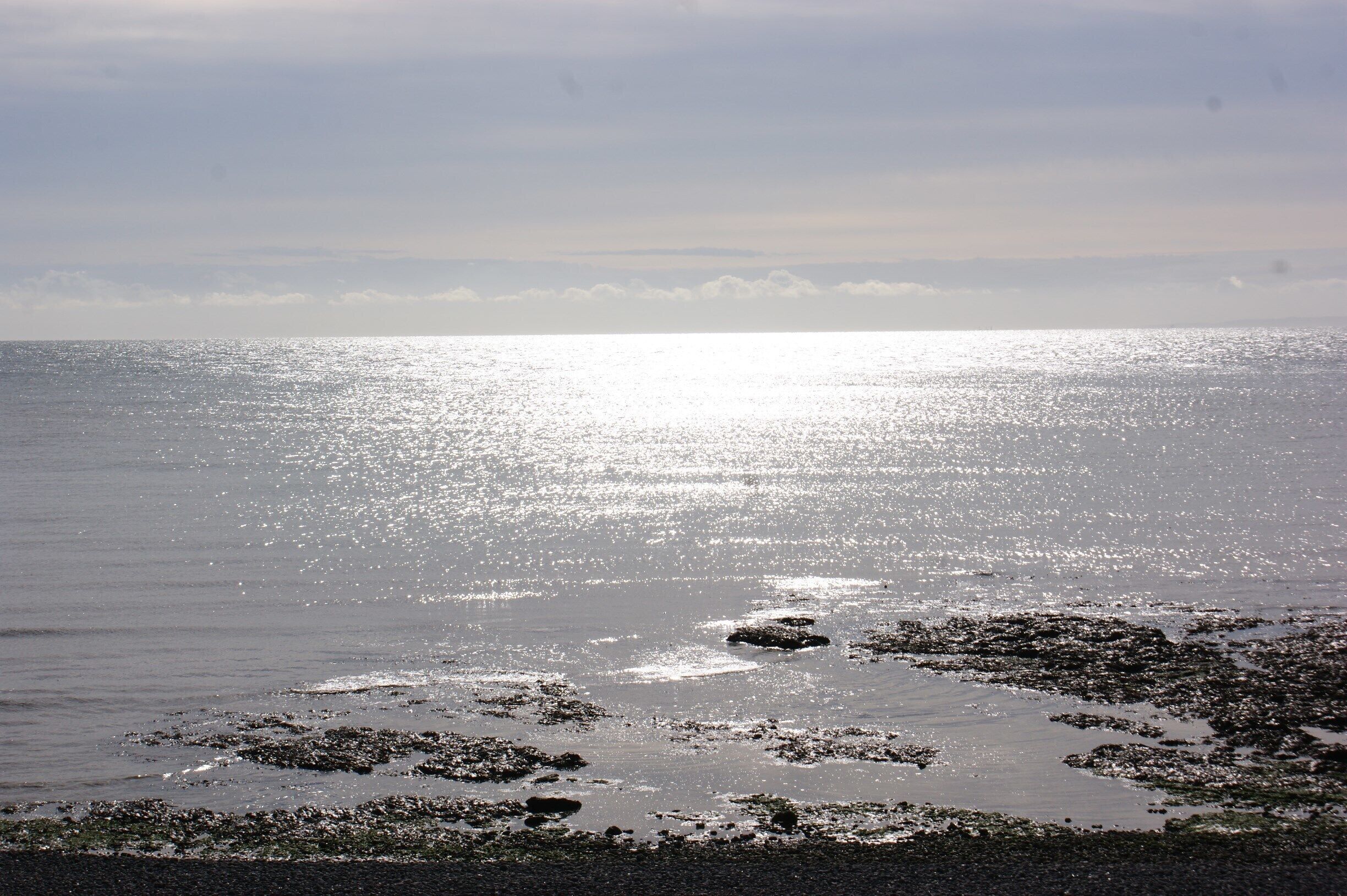 A beach with sunlight reflecting off the water and scattered rocks.