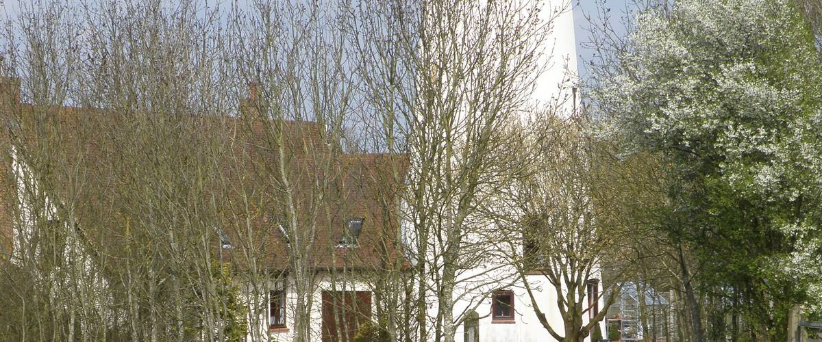 A white tower with a dark roof, surrounded by trees and a grassy field.