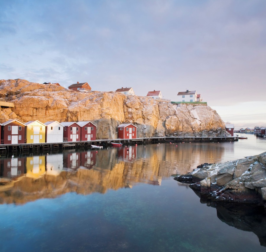 A coastal village with colorful wooden houses and a rocky cliff.