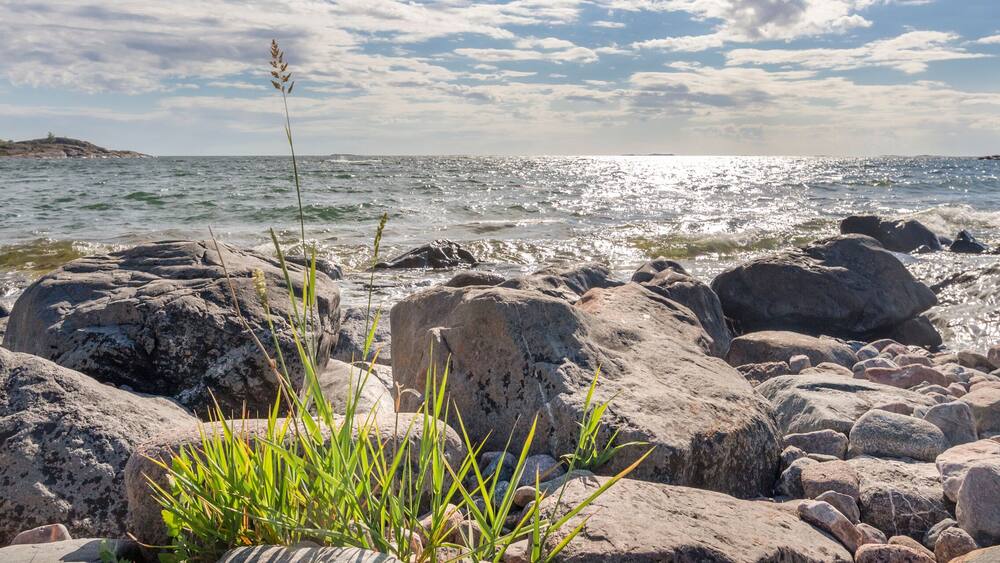 A rocky shoreline with waves crashing against the rocks under a partly cloudy sky.