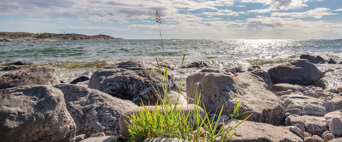 A rocky shoreline with waves crashing against the rocks under a partly cloudy sky.