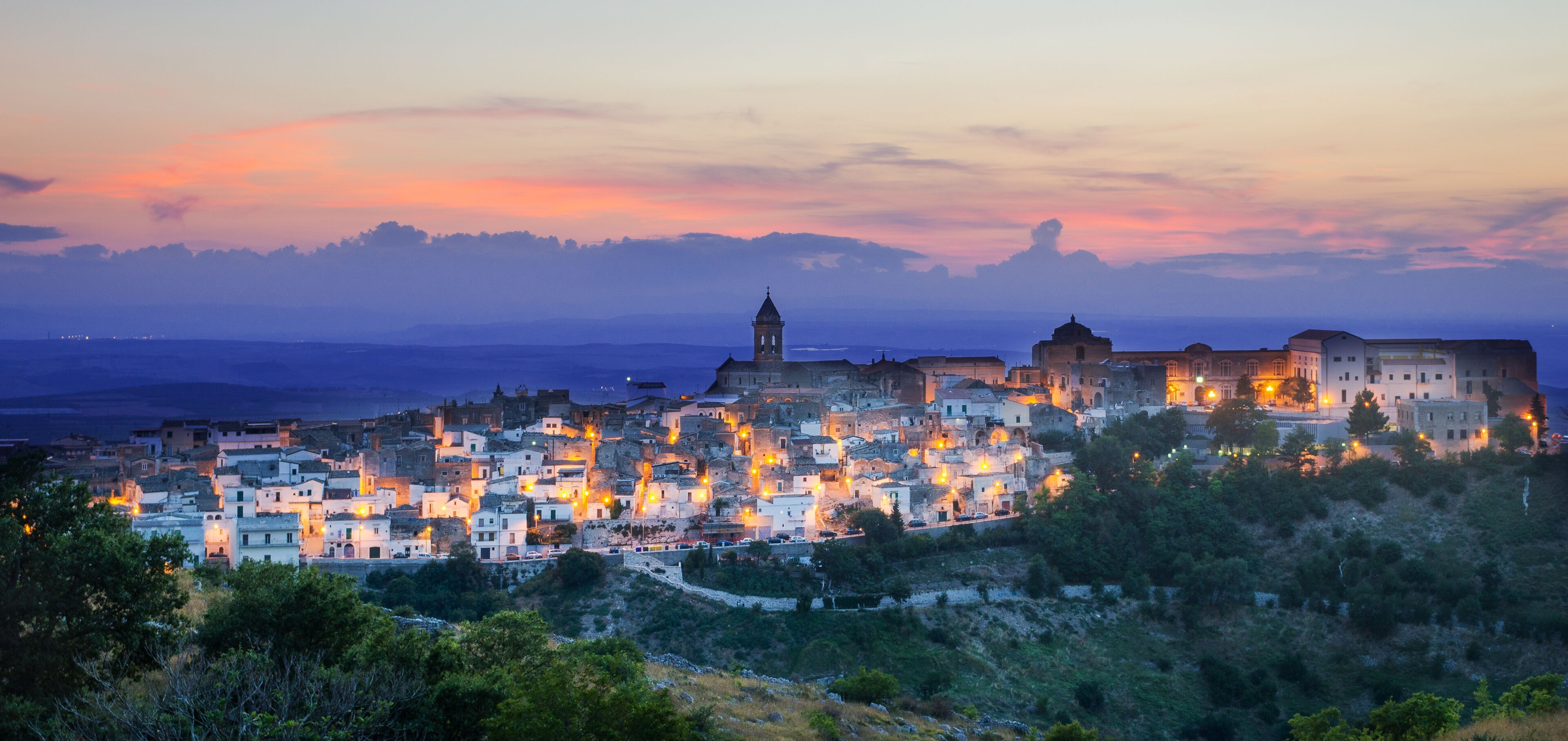 A coastal town at dusk with illuminated buildings and a prominent church tower.