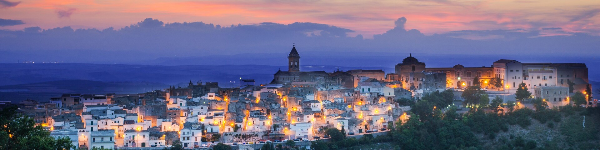 A coastal town at dusk with illuminated buildings and a prominent church tower.