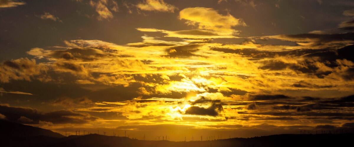 A sunset over a landscape with wind turbines silhouetted against the sky.