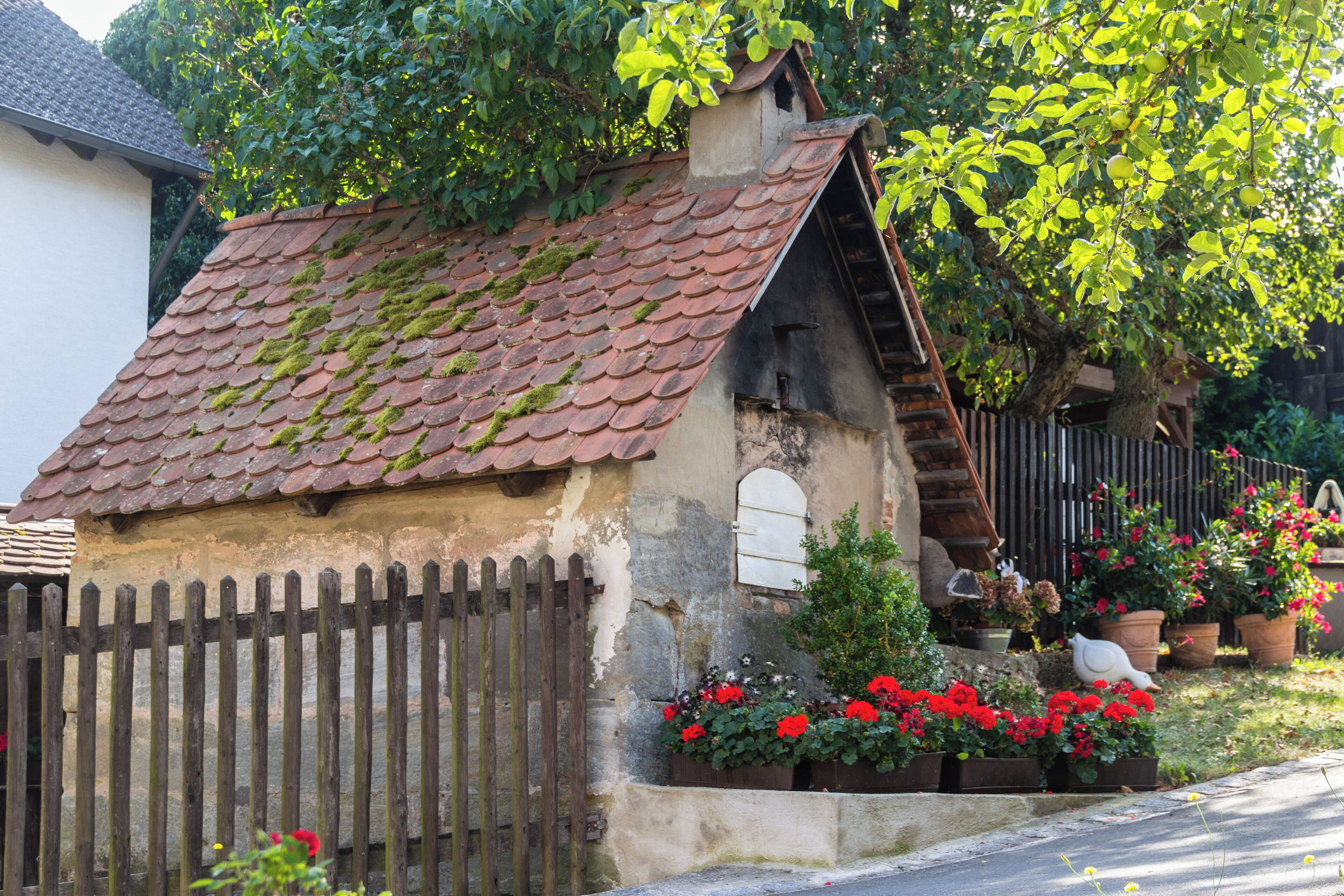A rustic house with a tiled roof, wooden fence, and blooming flowers.