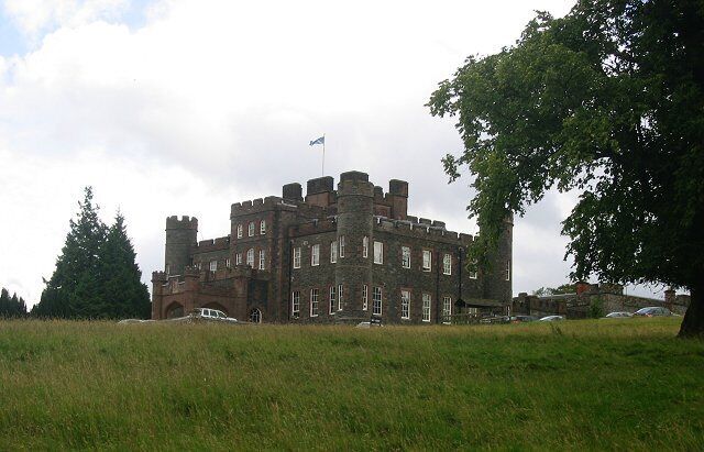 A large castle with multiple towers and a flag on top, surrounded by a grassy field and trees.