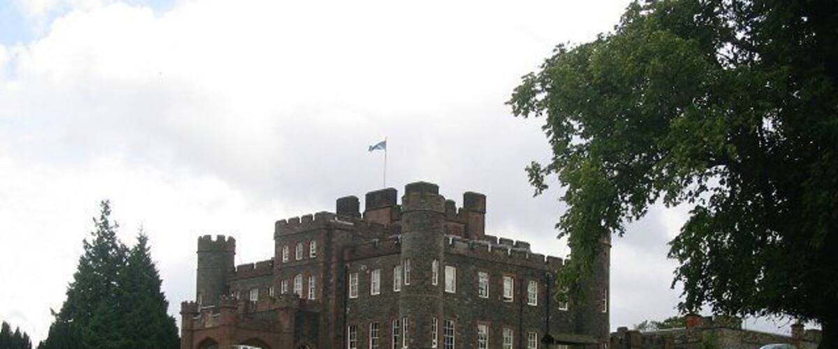 A large castle with multiple towers and a flag on top, surrounded by a grassy field and trees.