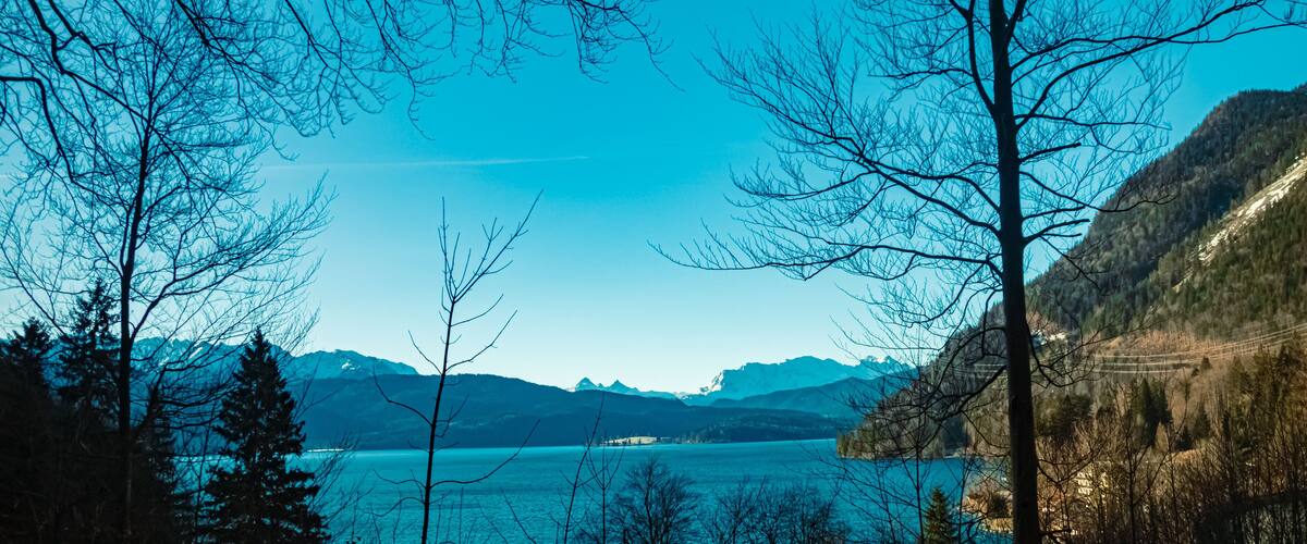 A lake surrounded by mountains and leafless trees.