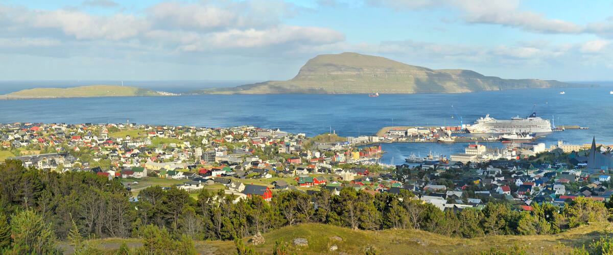 A coastal town with a prominent hill, a cruise ship docked at the harbor, and several boats in the water.
