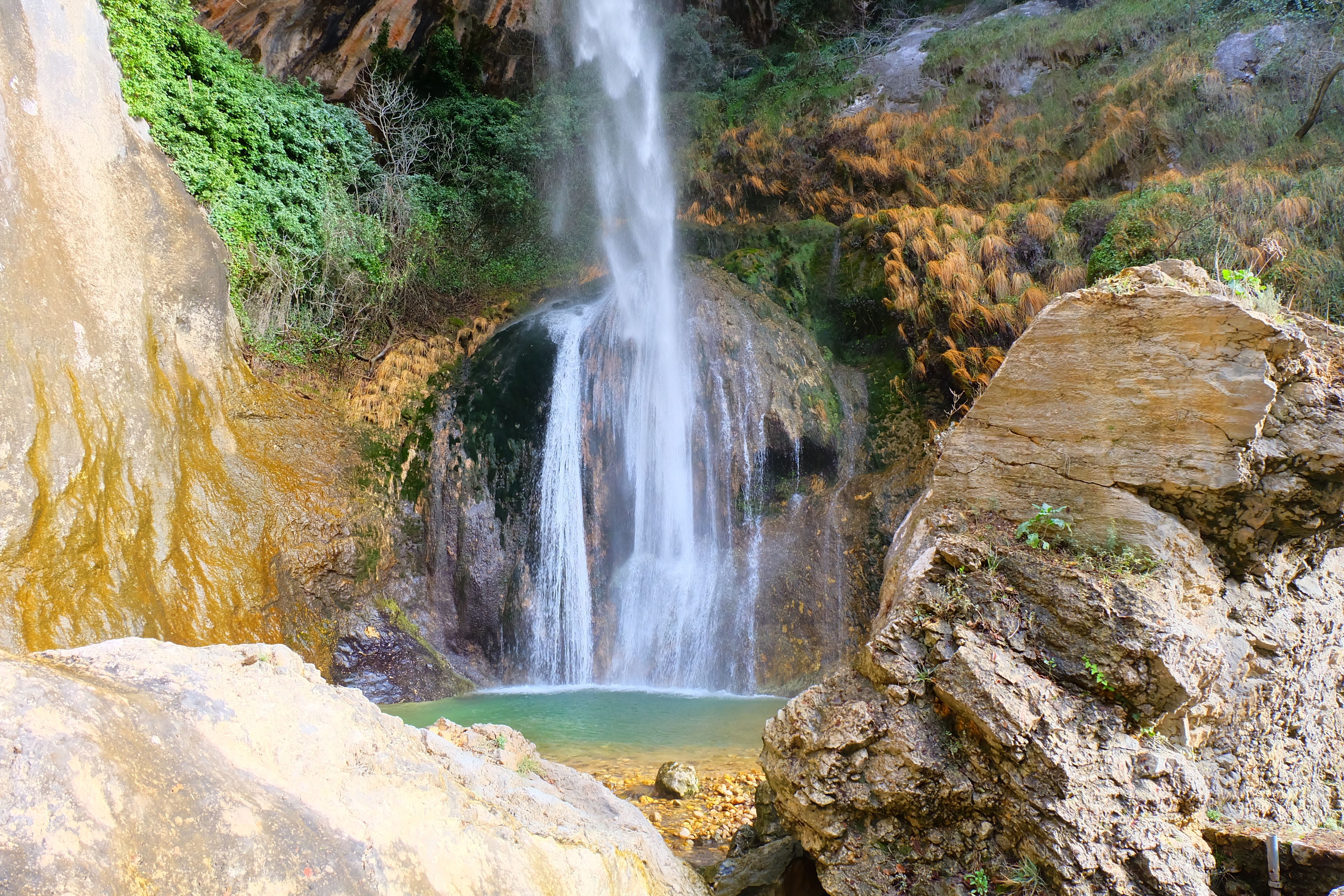 A waterfall cascading down a rocky cliff surrounded by lush greenery.