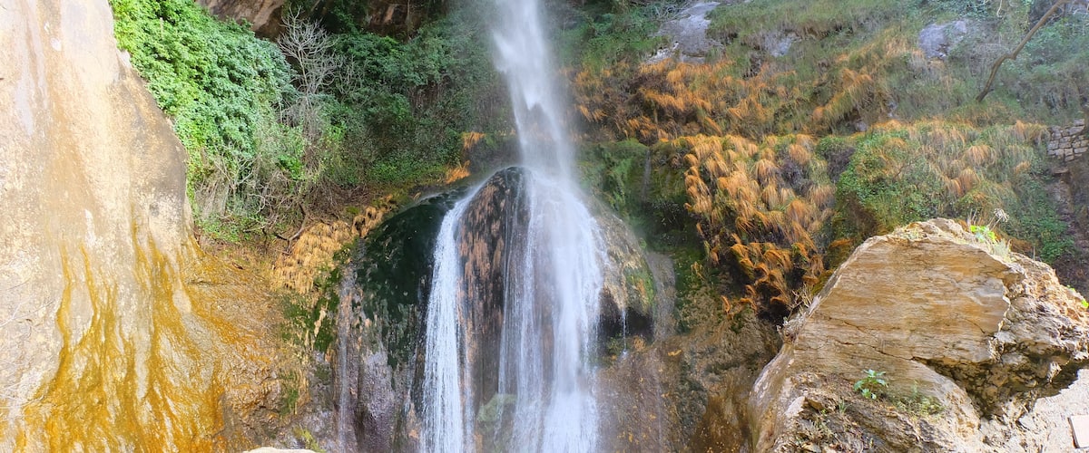 Una cascada se precipita por un risco rocoso, rodeada de abundante vegetación.