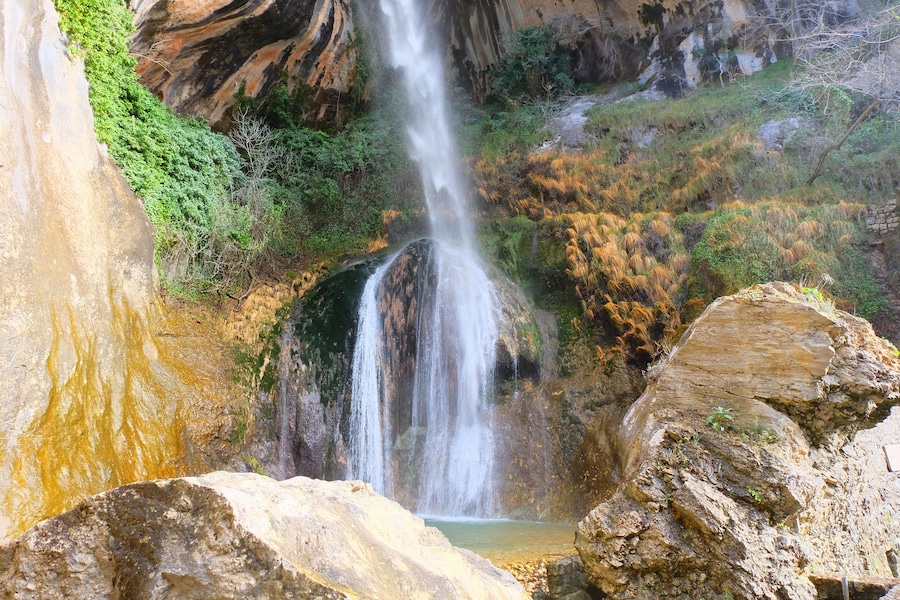 Una cascada se precipita por un risco rocoso, rodeada de abundante vegetación.