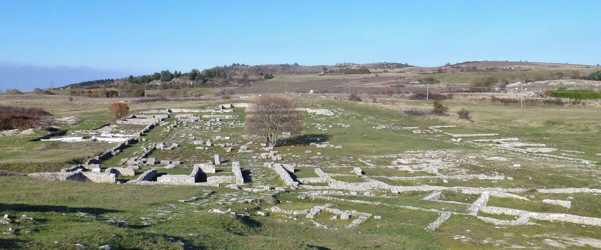 Ancient stone ruins in a grassy field with a clear sky.