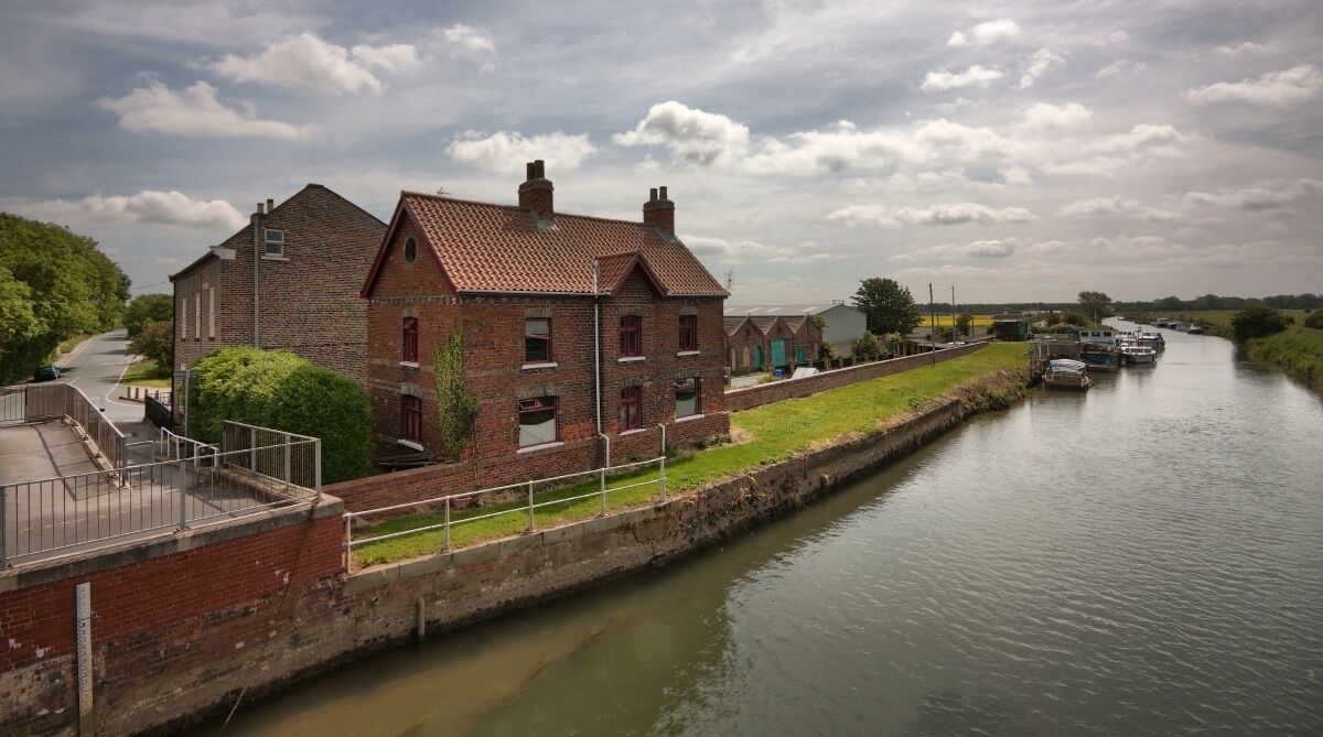 A brick building with a red-tiled roof beside a canal with boats.