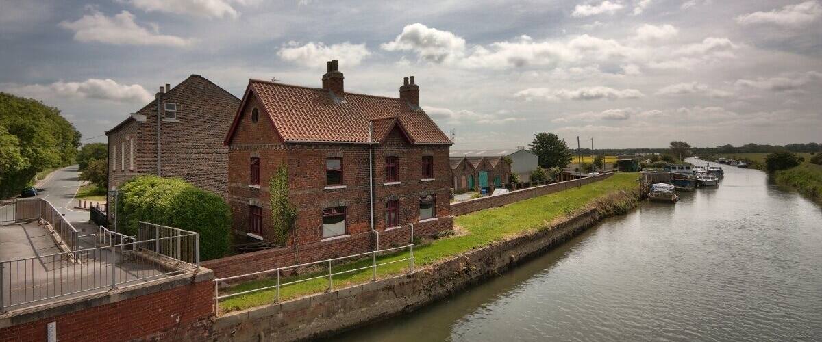 A brick building with a red-tiled roof beside a canal with boats.