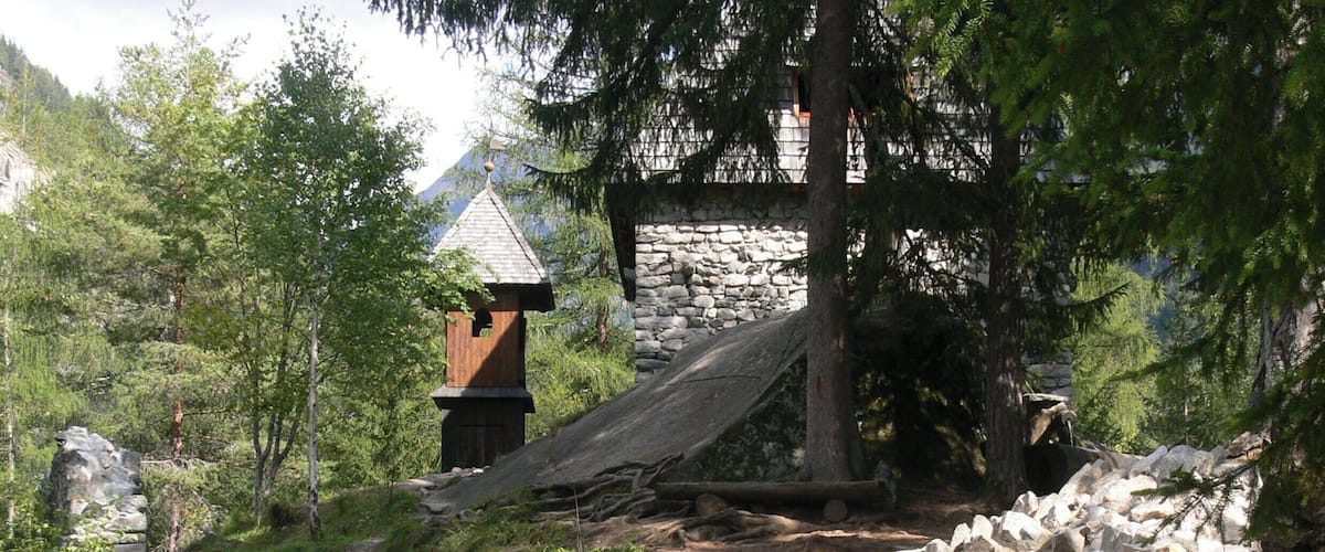 A stone wall, a wooden structure, and a forested area with a mountain in the background.