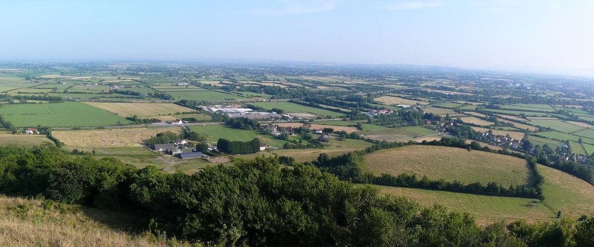 A panoramic view of a rural landscape with rolling hills, scattered fields, and small clusters of houses.