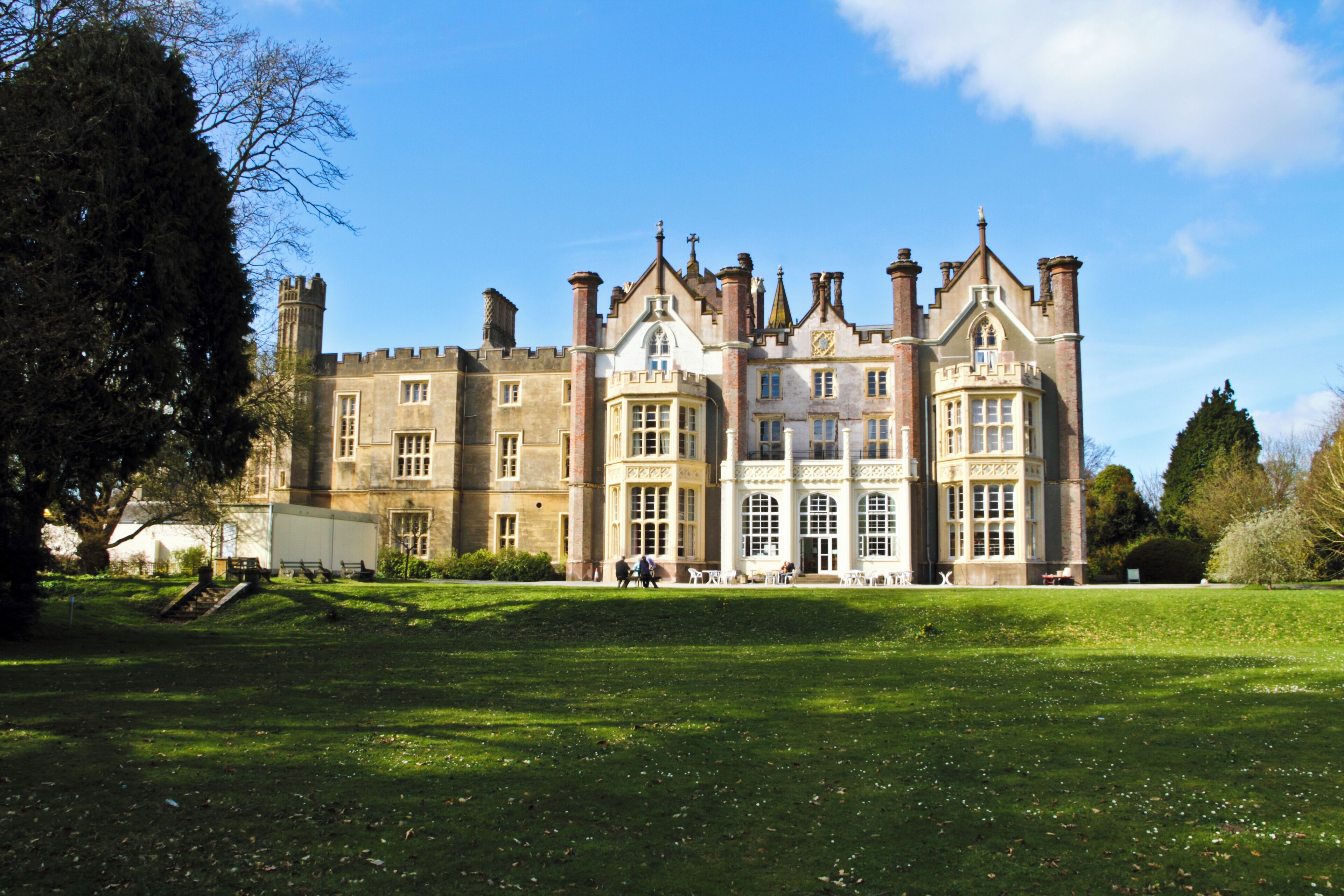 A large, historic building with multiple towers and a well-maintained lawn in front.