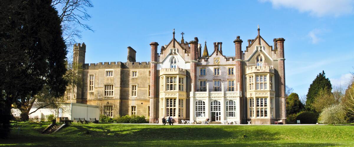 A large, historic building with multiple towers and a well-maintained lawn in front.