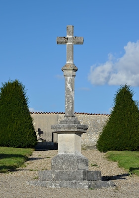 A stone cross monument in a grassy area with a building in the background.