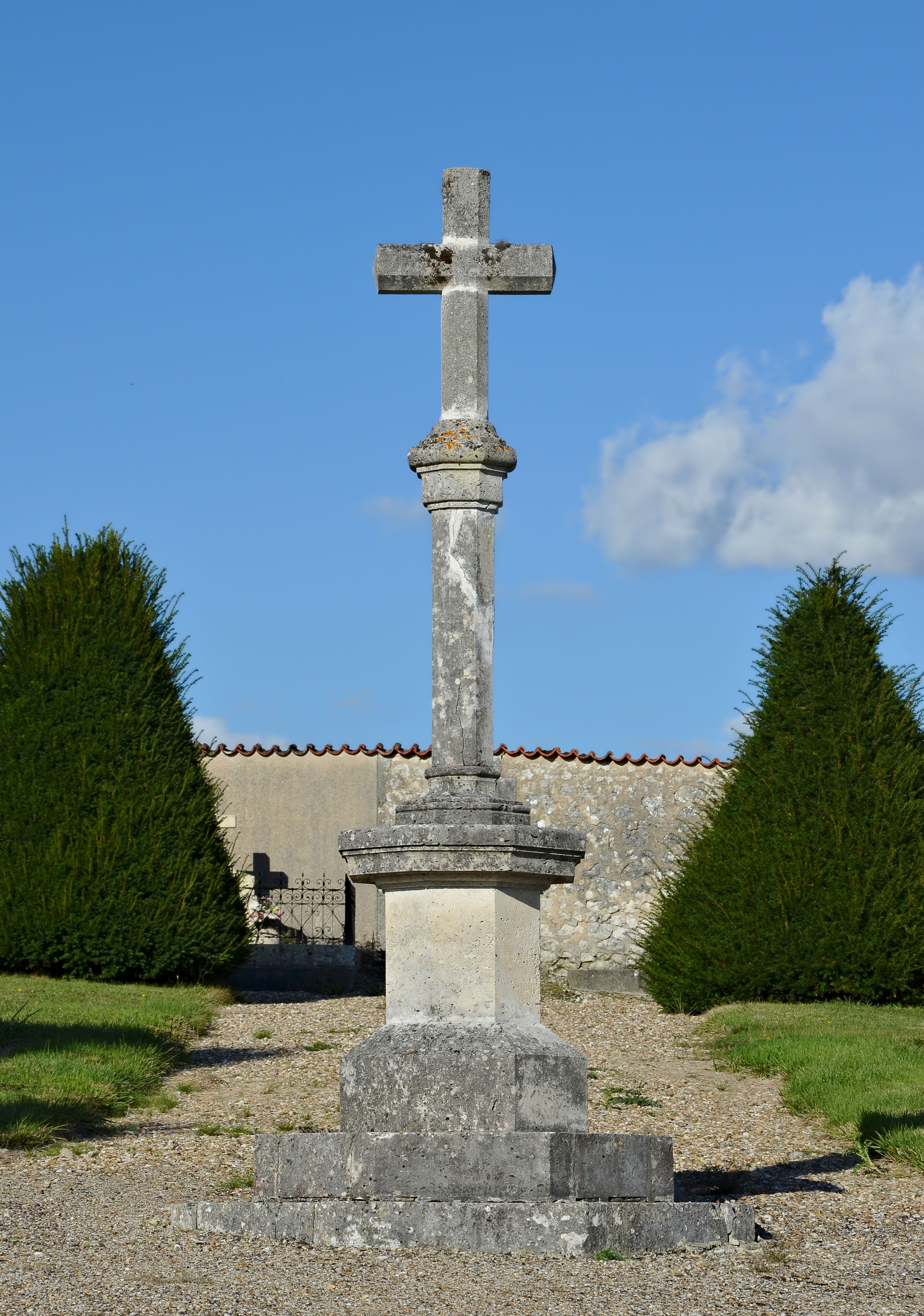 A stone cross monument in a grassy area with a building in the background.