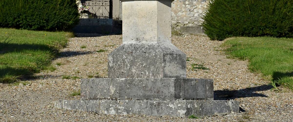 A stone cross monument in a grassy area with a building in the background.