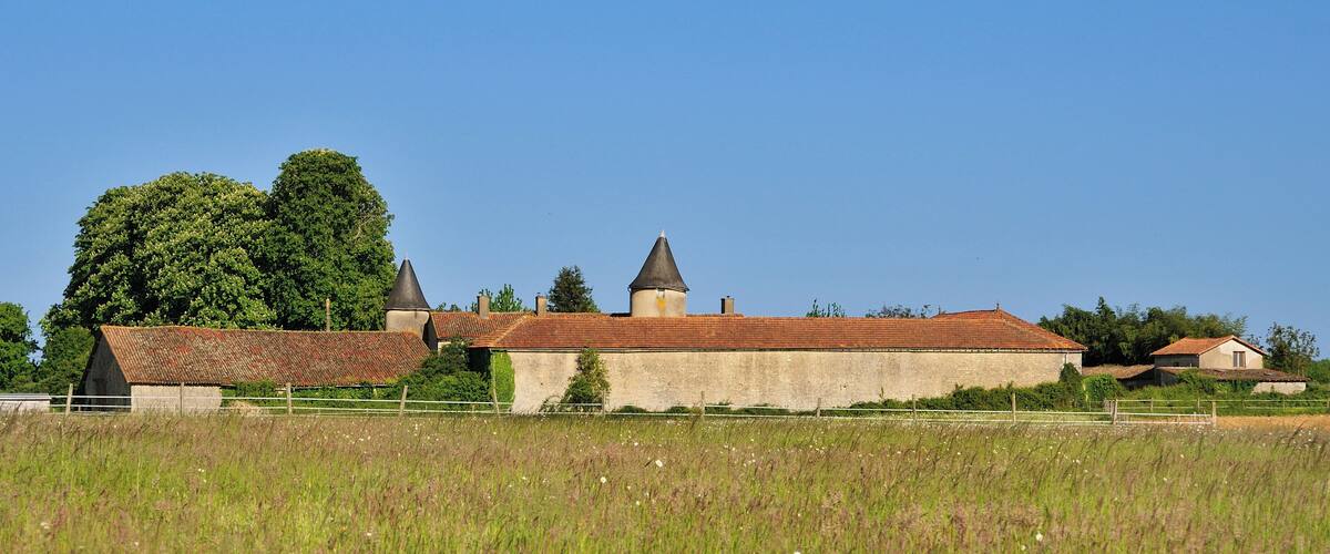 A rural landscape with a large field, a farmhouse, and a church with a bell tower.