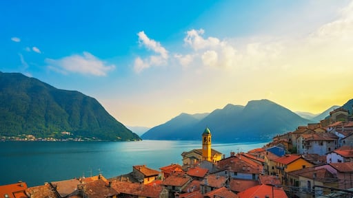 Una cittadina costiera con edifici dai tetti rossi, un'imponente torre gialla e montagne sullo sfondo.